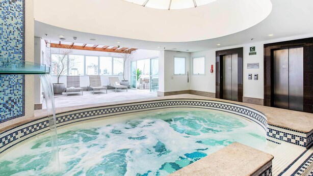 Un área de piscina interior moderna con una vista despejada del paisaje urbano a través de amplias ventanas.