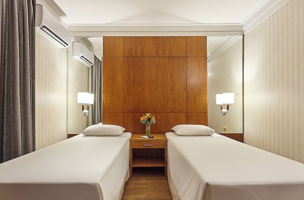 A hotel room with two beds, a wooden headboard, bedside lamps, a nightstand with a vase of flowers, and a mirror. - Hotel Cassino Tower Campinas Cambui By Nacional Inn (Campinas)