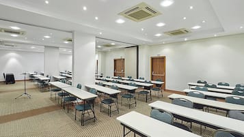 Un salón de conferencias con varias mesas y sillas, paredes blancas e iluminación en el techo.