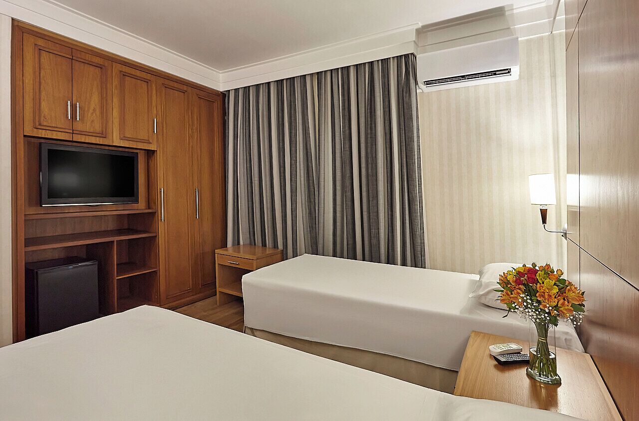 A hotel room with two beds, a TV, a desk, and a small table with a vase of flowers.