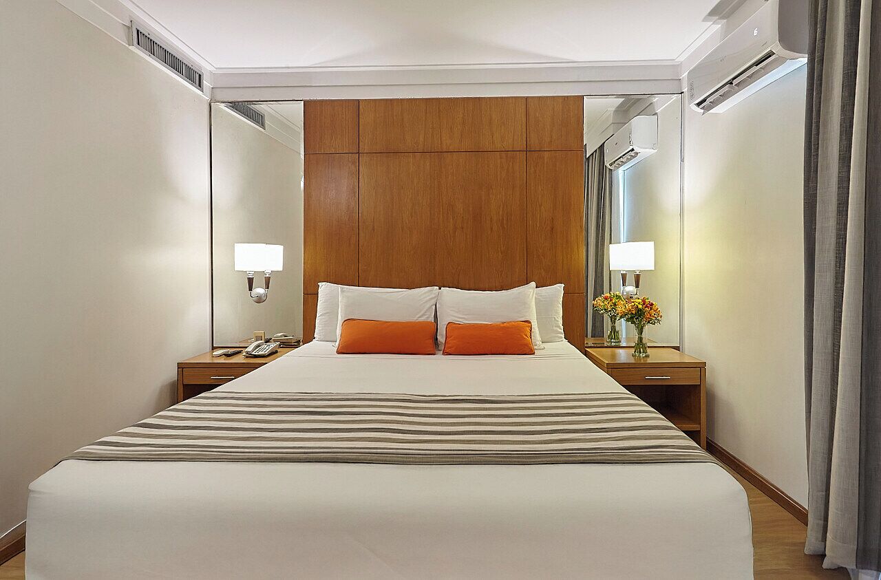 A hotel room with a large bed, two bedside tables, a mirror, and a nightstand with a lamp.