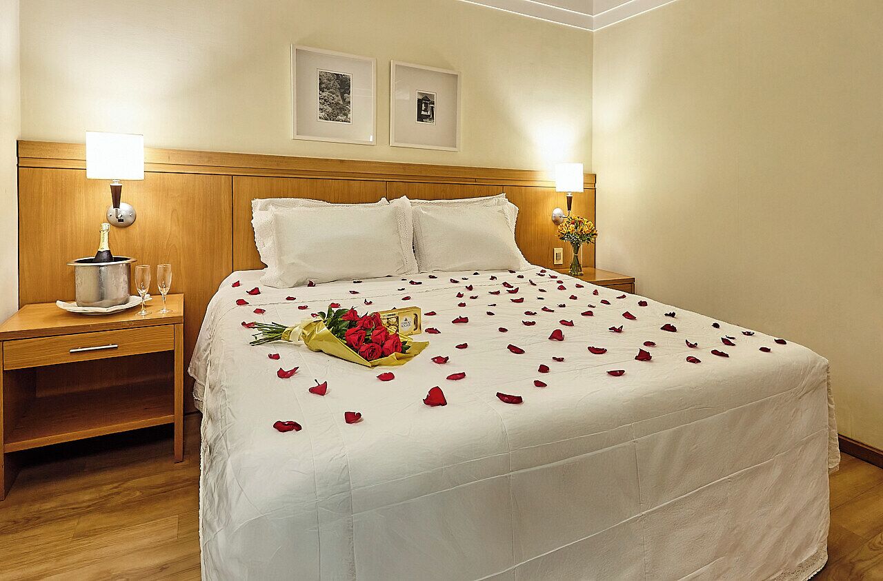 A hotel room with a large bed, two bedside tables, a nightstand, and a wall-mounted lamp.