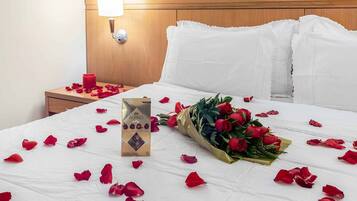 Une chambre d’hôtel avec un lit bien fait, une table de chevet avec une lampe et un bouquet de roses posé sur le lit.