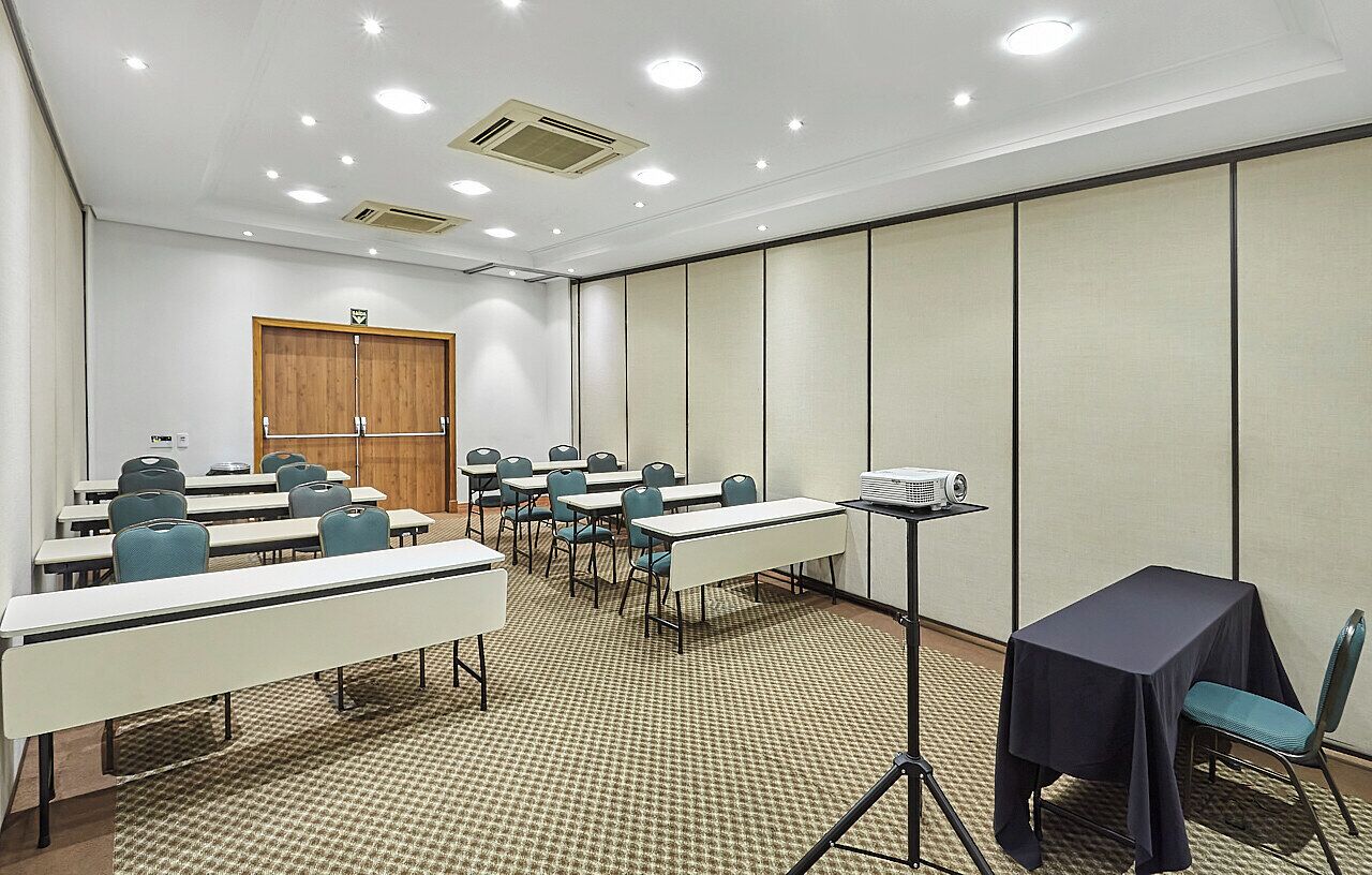 Un salón de conferencias con mesas, sillas, un atril y un proyector.