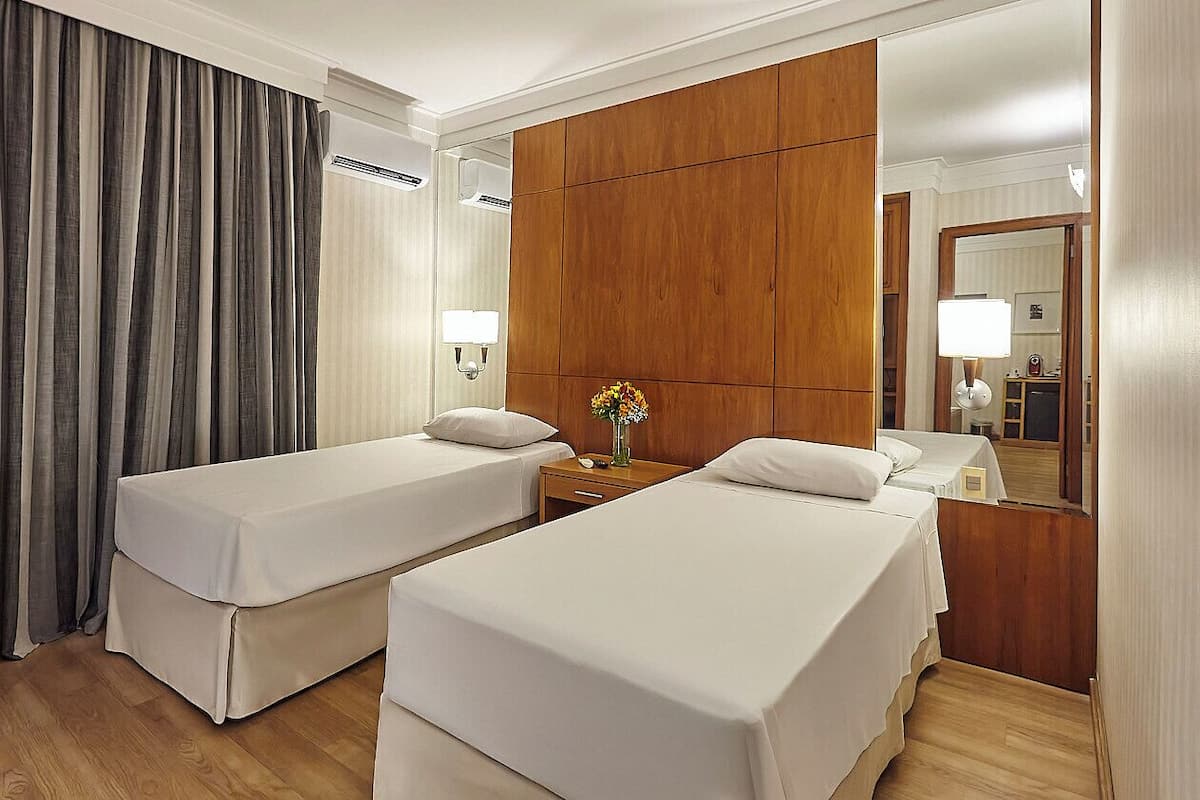 A hotel room with two beds, a wooden panel wall, a mirror, and a nightstand with a lamp.