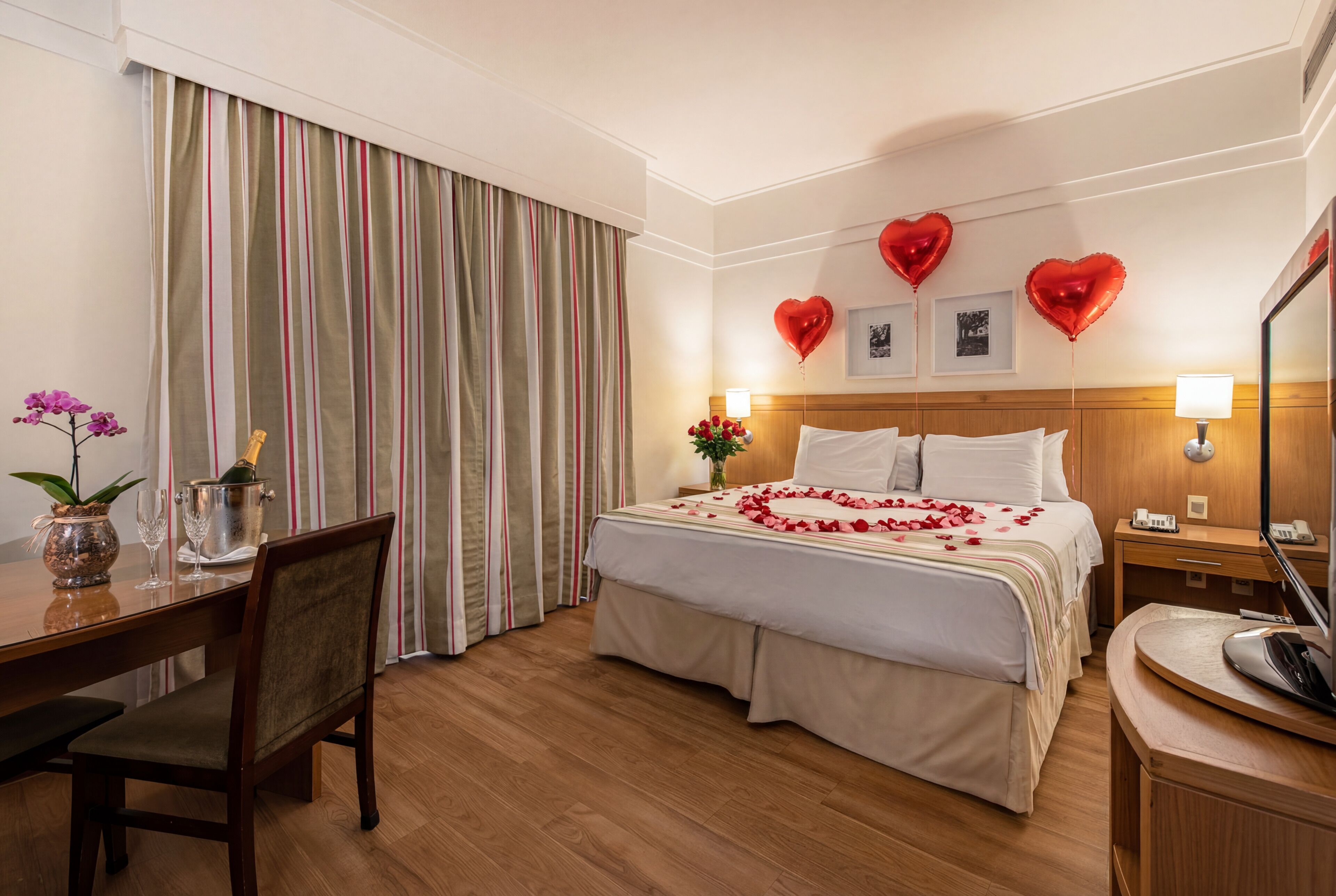 A hotel room with a bed, a desk, a chair, a dining table, and a large window with curtains.