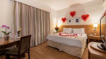 Habitación de hotel con cama, escritorio, silla, mesa de comedor y un ventanal con cortinas.