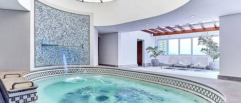 A modern indoor pool area with a mosaic wall, lounge chairs, and a skylight.