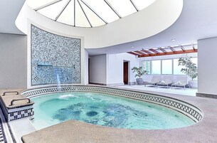 Un área de piscina interior moderna con un muro de mosaicos, sillones de descanso y tragaluces.