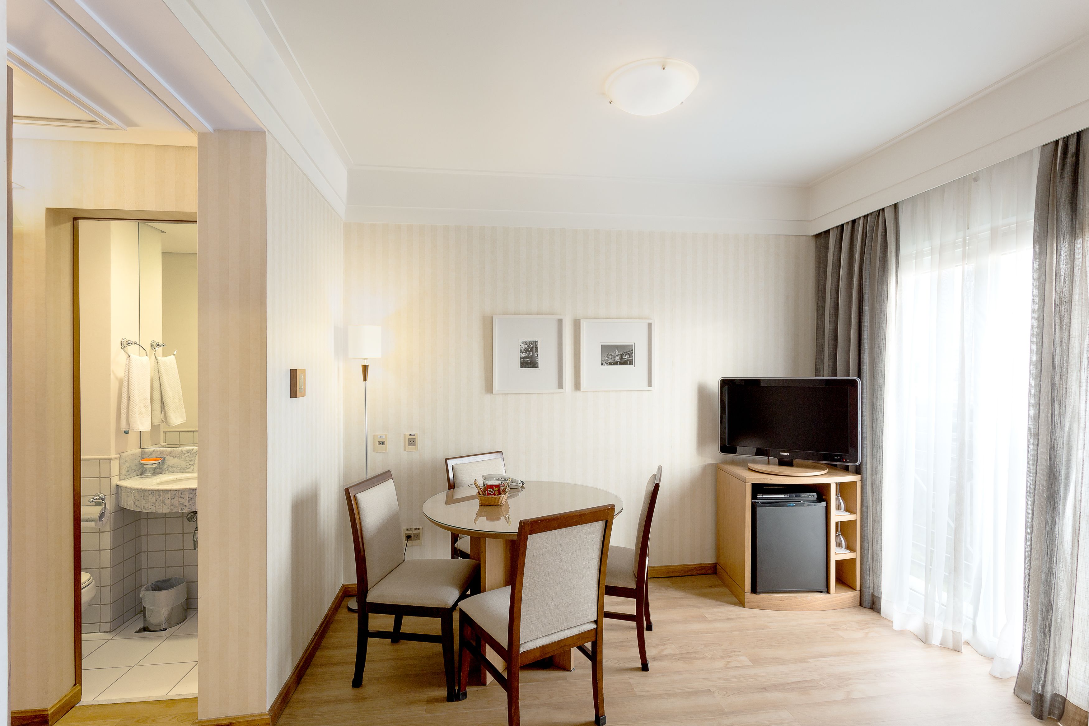 Una habitación de hotel con una mesa de comedor, sillas, un televisor y una pequeña cocina.