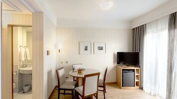 Una habitación de hotel con una mesa de comedor, sillas, un televisor y una pequeña cocina.