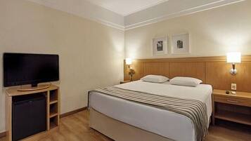 A hotel room with a bed, bedside tables, a television, and wall-mounted lamps.
