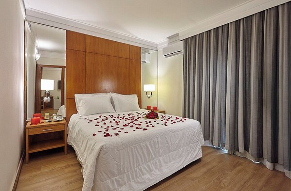 Una habitación de hotel con una cama grande, cabecero de madera, mesita de noche con lámpara y un espejo.
