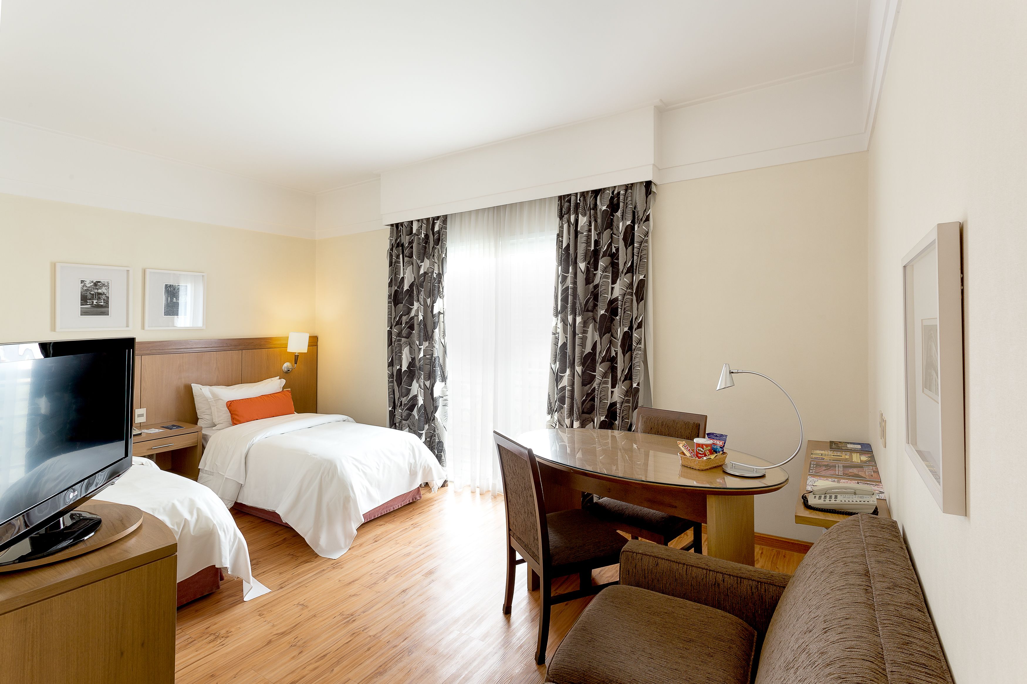 A hotel room with a bed, a desk with a lamp, a television, and a sofa.