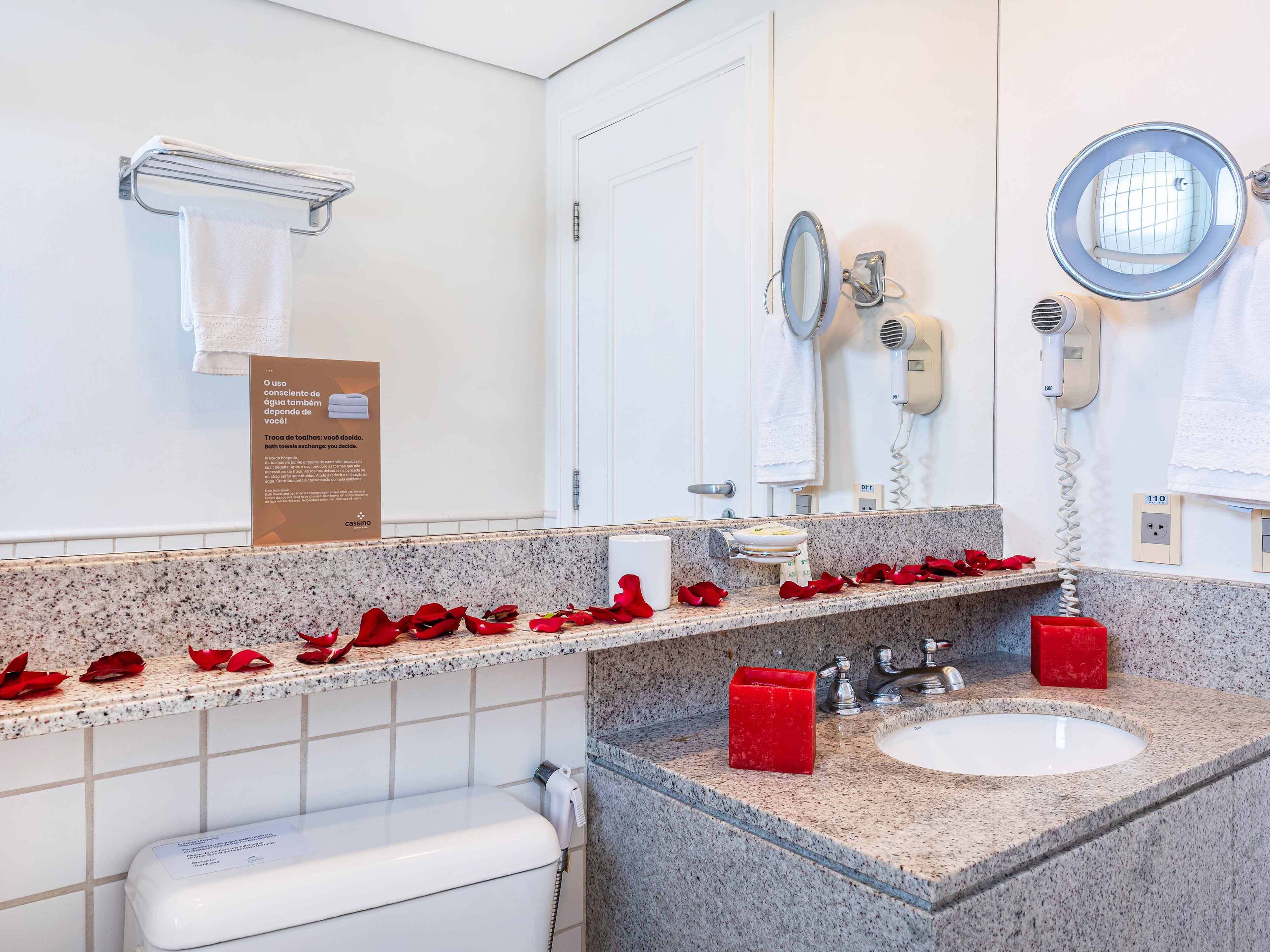 A bathroom with a granite countertop, two sinks, a toilet, a towel rack, a mirror, and a hairdryer.