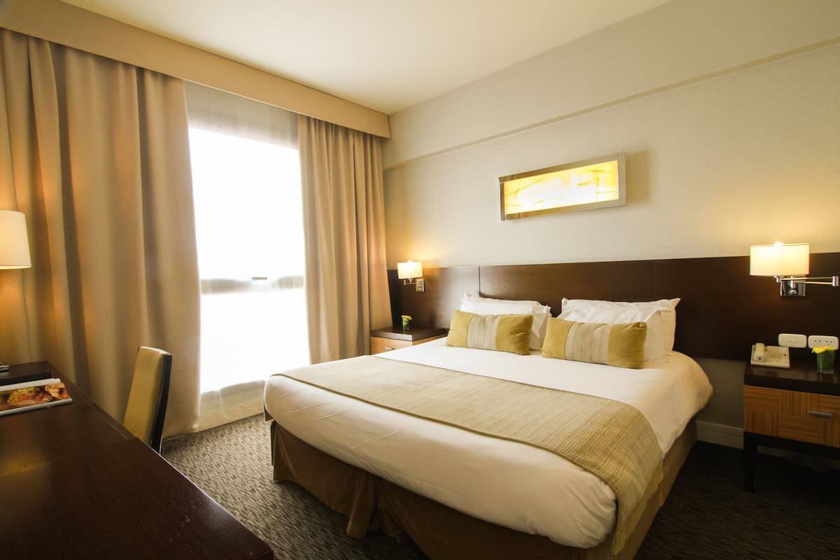 A hotel room with a large bed, a desk, a chair, a nightstand, and a lamp.