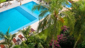 Una piscina con sillas de descanso y sombrillas, rodeada de exuberante vegetación y vistas a un río.