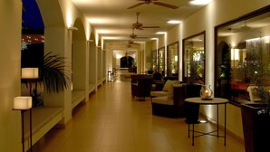 Un pasillo de hotel con ventiladores de techo, zonas de estar y ventanas amplias.