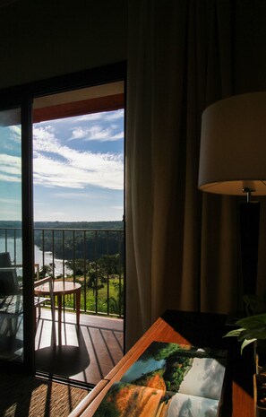 Quarto com vista para um lago e montanhas, uma mesa com cadeiras e um abajur.