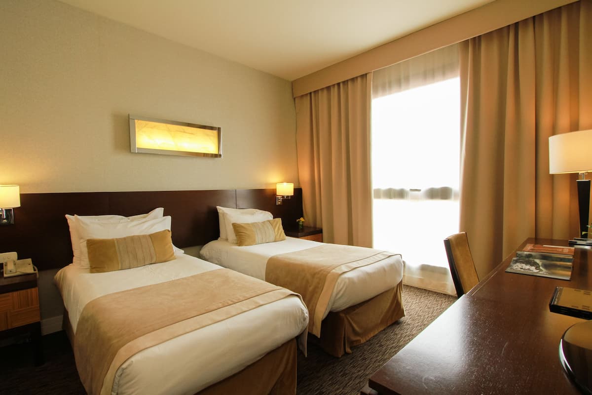 A hotel room with two beds, a desk, and a large window with curtains.