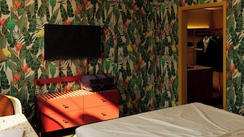 Hotellihuone, jossa on sänky, punainen lipasto, seinälle asennettu televisio ja vaatekaappi, jossa on henkarissa olevia vaatteita.