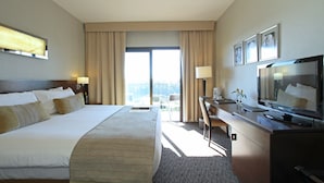 A hotel room with a large bed, a desk with a computer, a television, and a view of the outdoors. - Panoramic Grand Hotel (Puerto Iguazú)