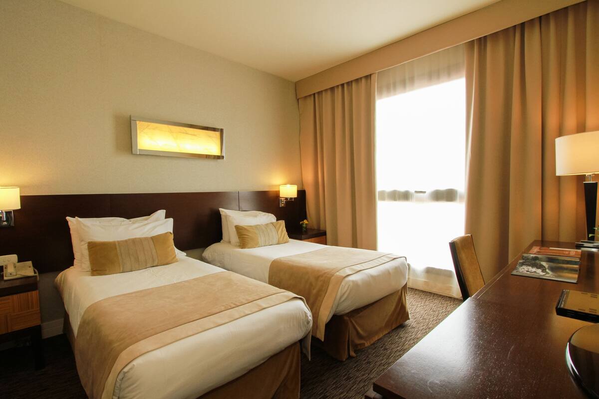 A hotel room with two beds, a desk, and a large window with curtains.