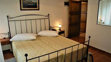 A bedroom with a bed, bedside table, lamp, and a door leading to another room.