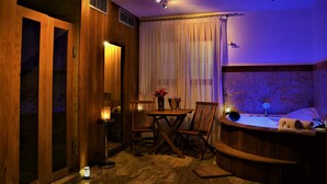 A cozy room with a wooden floor, a small table with chairs, a candle, a bathtub, and a curtain.