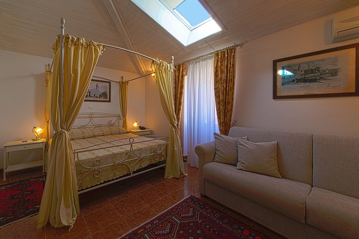 Een slaapkamer met een hemelbed, een bank, een dakraam en een ingelijste foto aan de muur.