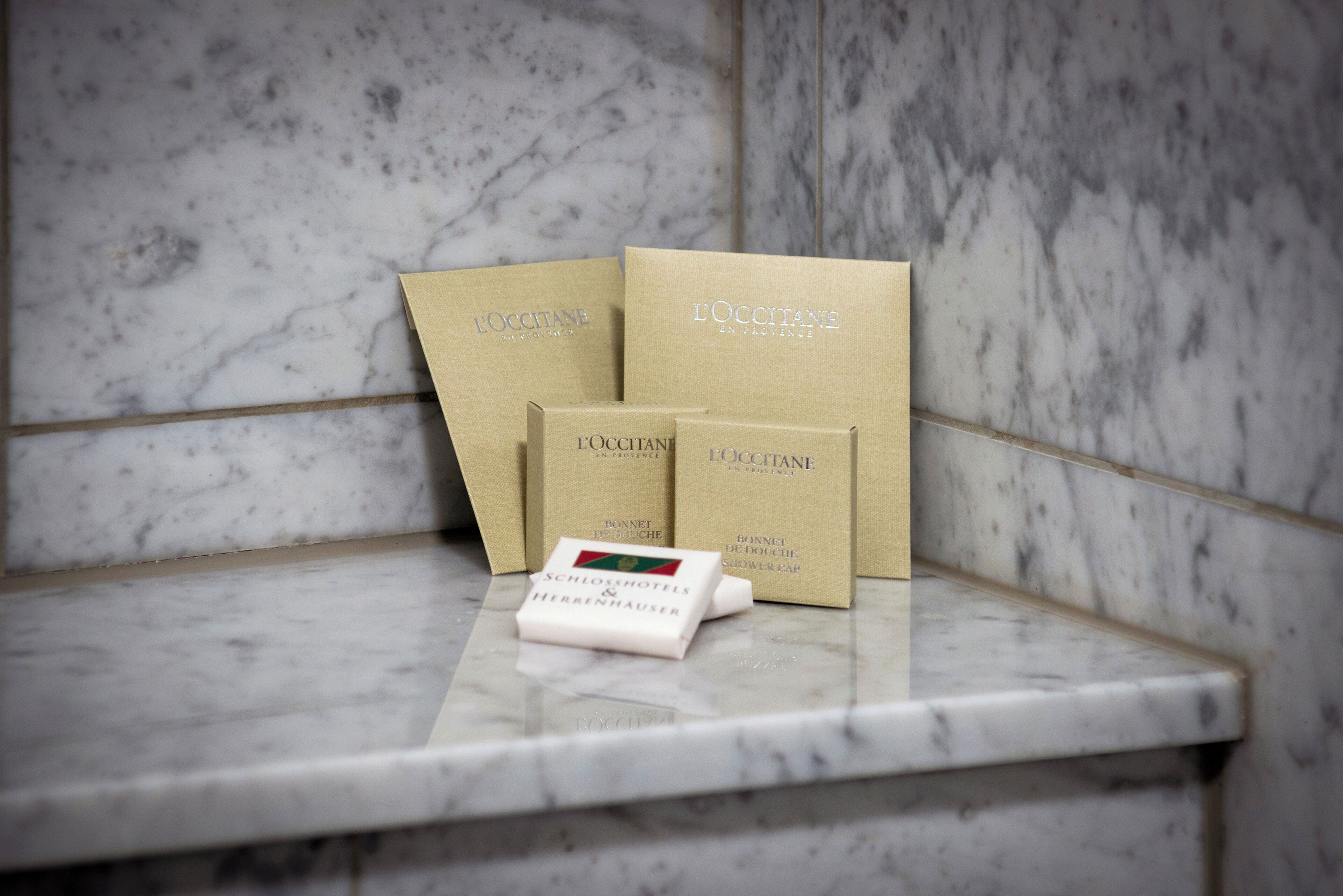 Tre presentförpackningar från L'OCCITANE en Provence och en duschmössa placerade på en marmoryta.