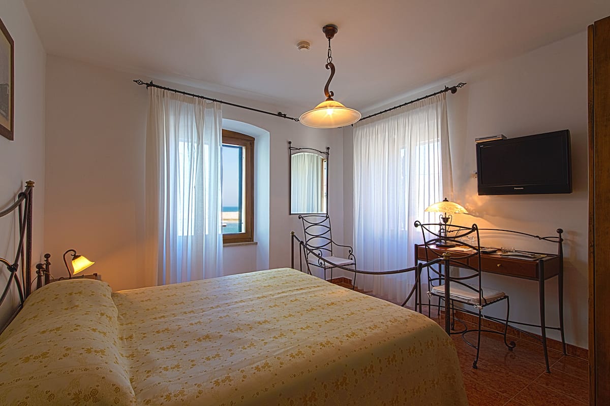 Een slaapkamer met een bed, een bureau met stoel, een televisie en een raam met gordijnen.