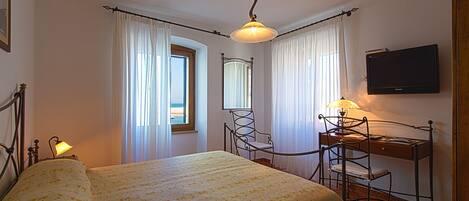 A hotel room with a bed, a desk with a chair, a television, and a window with curtains.