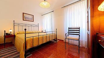 Un dormitorio con estructura de cama metálica, una silla, una mesita de noche con lámpara y un cuadro enmarcado en la pared.