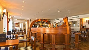 A bar area with wooden stools and tables, a bar counter with bottles, and a nautical-themed decor.
