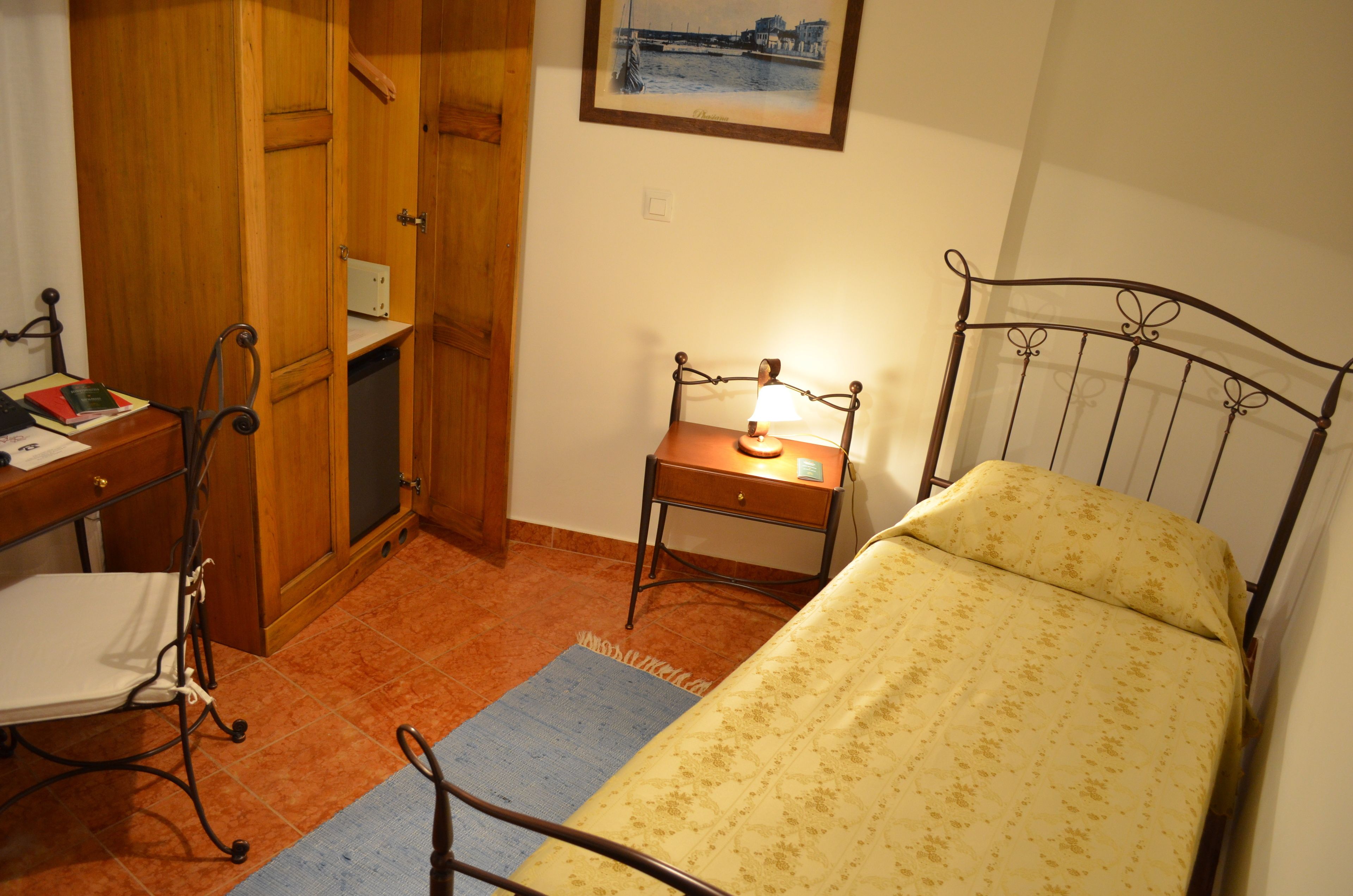 Een slaapkamer met een bed, een bureau met stoel, een bijzettafeltje met lamp en een kledingkast.