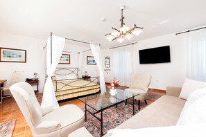Quarto com uma cama, mesa de centro de vidro, uma cadeira, televisão e um candelabro.