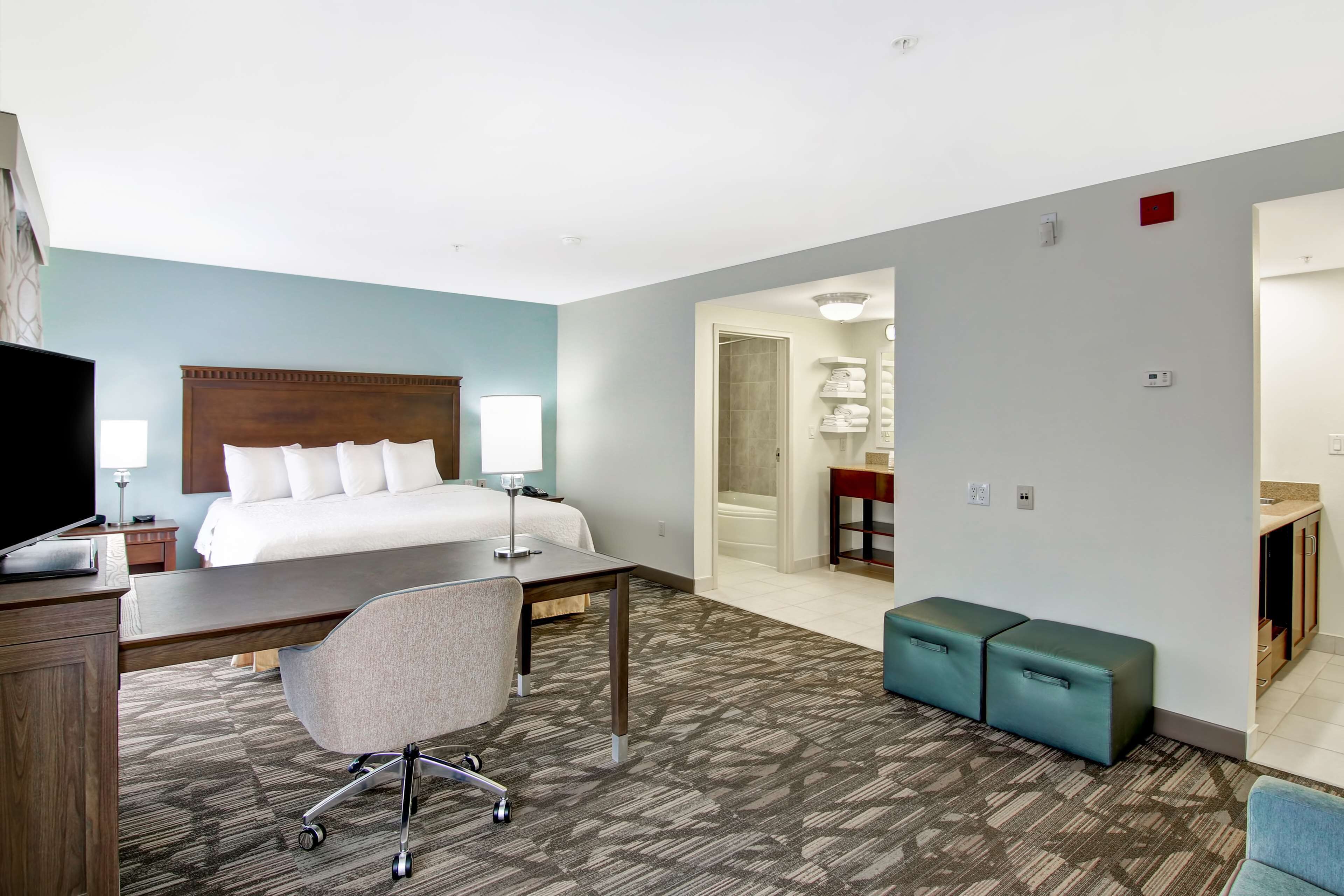 A hotel room with a bed, desk, chair, and a small seating area.