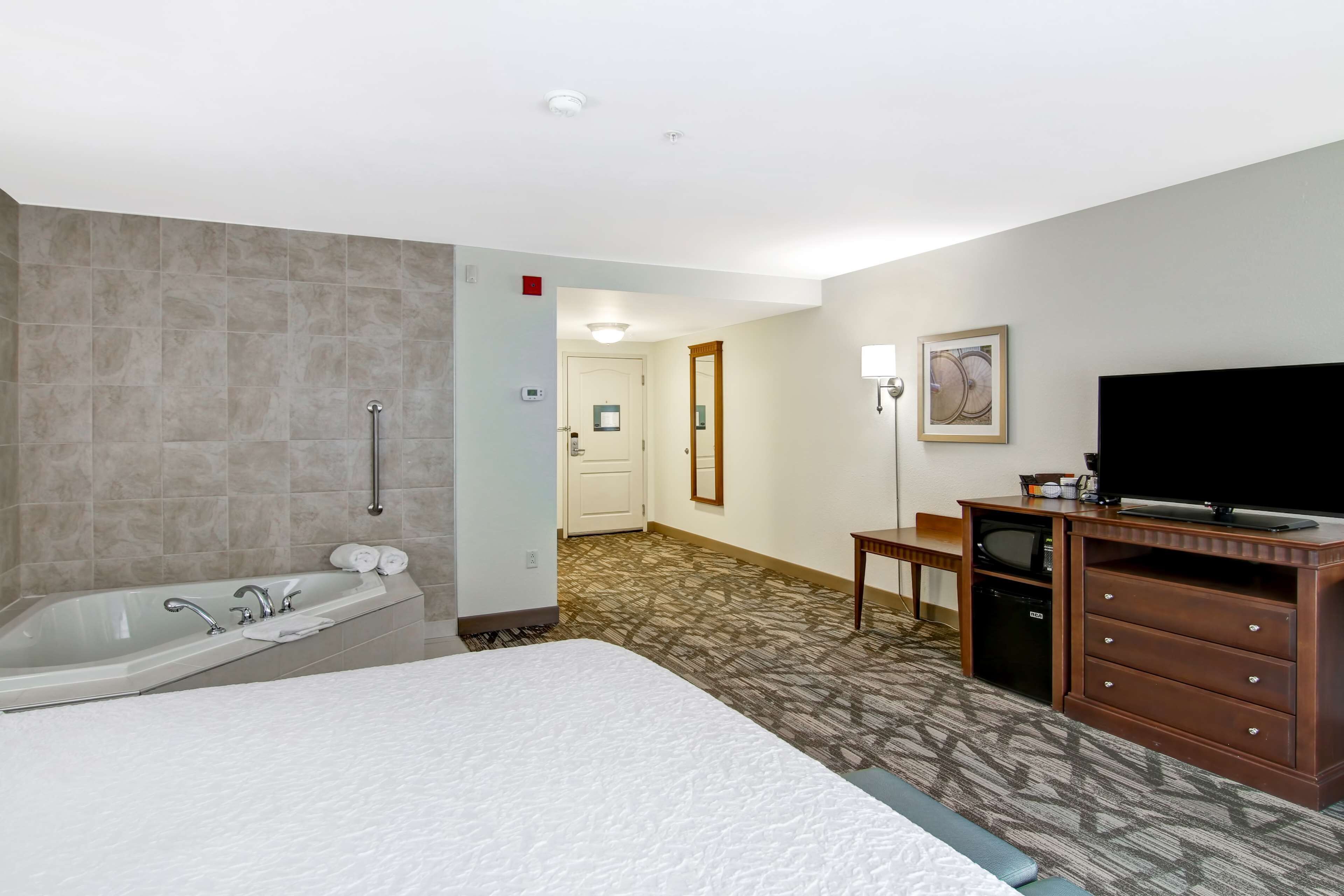 Une chambre d’hôtel avec un grand lit, une baignoire, un bureau avec une télévision et une porte donnant sur une autre pièce.