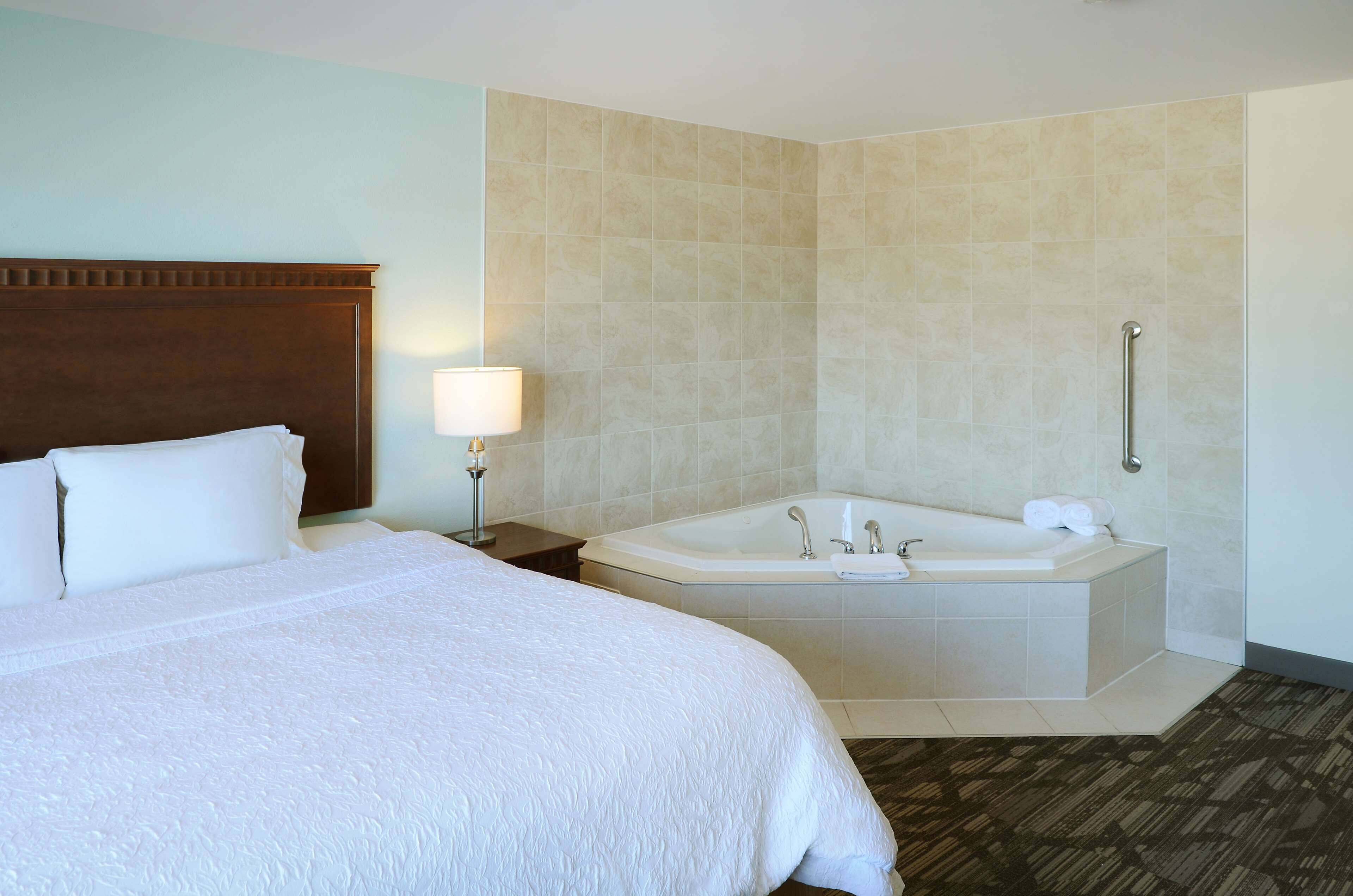 A hotel room with a large bed, a separate bathroom with a bathtub, and a handrail for accessibility.