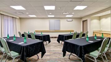 Ein Konferenzraum mit vier Tischen, jeder mit einer schwarzen Tischdecke und grünen Stühlen. Auf den Tischen stehen Wasserflaschen und an der Wand eine große Whiteboard-Tafel.