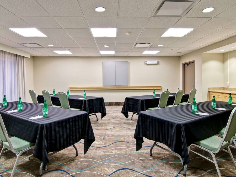 Ein Konferenzraum mit vier Tischen, jeder mit einer schwarzen Tischdecke und grünen Stühlen. Auf den Tischen stehen Wasserflaschen und an der Wand eine große Whiteboard-Tafel.