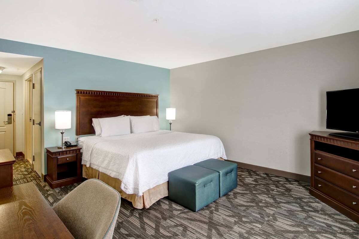 A hotel room with a large bed, bedside tables, a TV, and a desk.