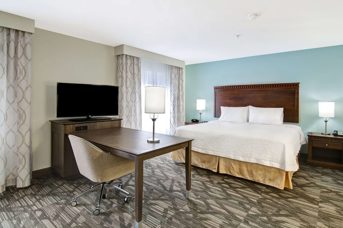 A hotel room with a bed, a desk with a chair, a TV, and two bedside lamps.