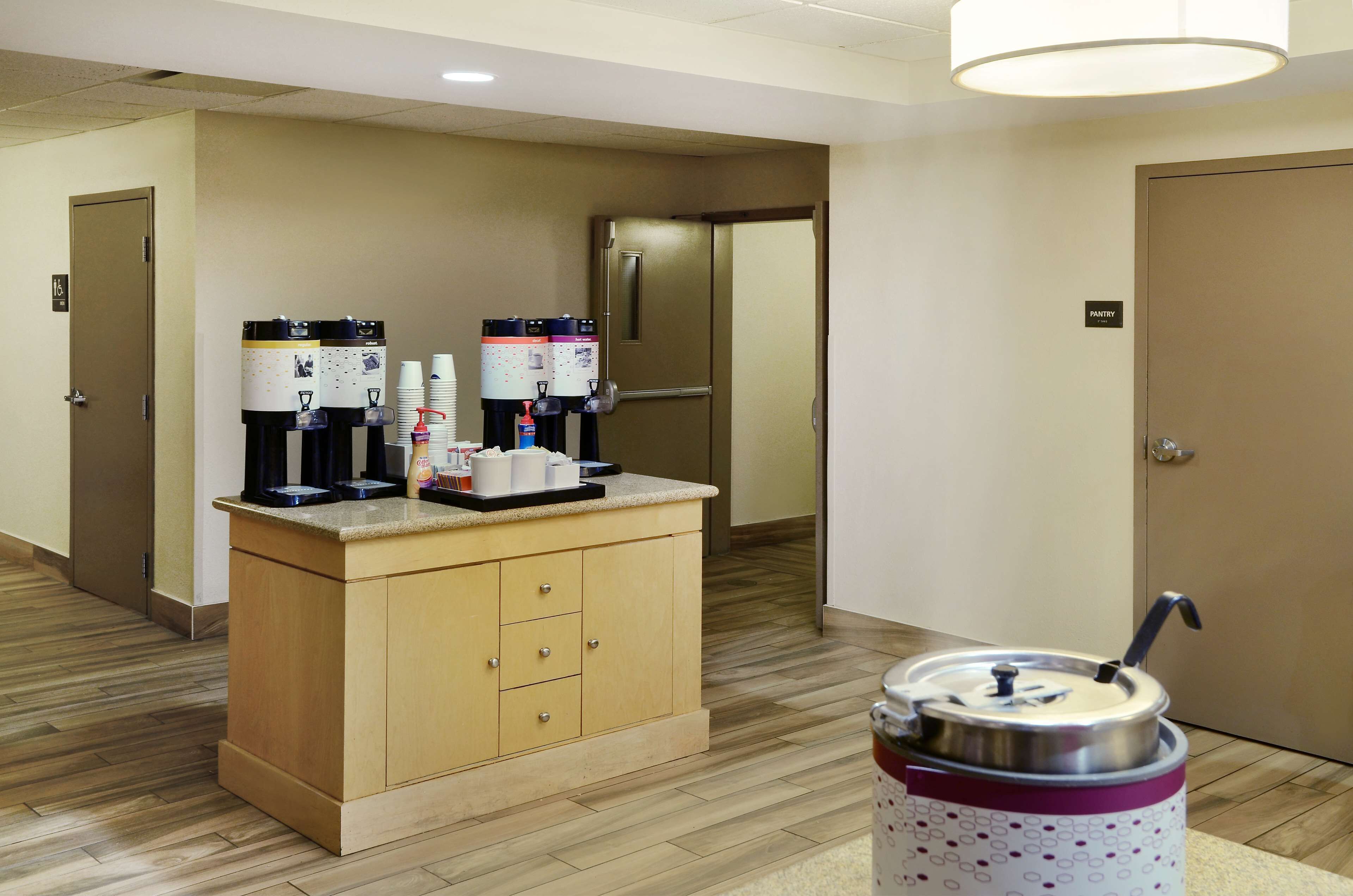 A hotel room with a kitchenette area featuring a coffee machine, a water dispenser, and a trash can.
