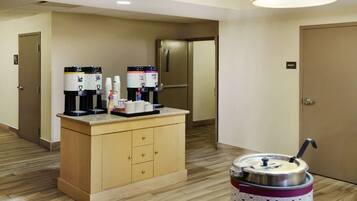A hotel room with a kitchenette area featuring a coffee machine, a water dispenser, and a trash can.