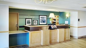 A reception desk with a 'Welcome to Saint John' sign, framed photographs, a lamp, and a 'Tim Hortons' sign. - Hampton Inn & Suites Saint John (Saint John)