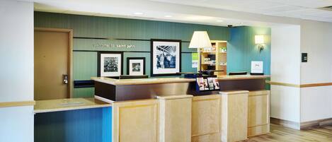 A reception desk with a 'Welcome to Saint John' sign, framed photographs, a lamp, and a 'Tim Hortons' sign.