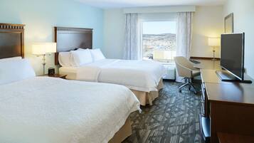 A hotel room with two beds, a desk, a chair, a TV, and a window with a city view.