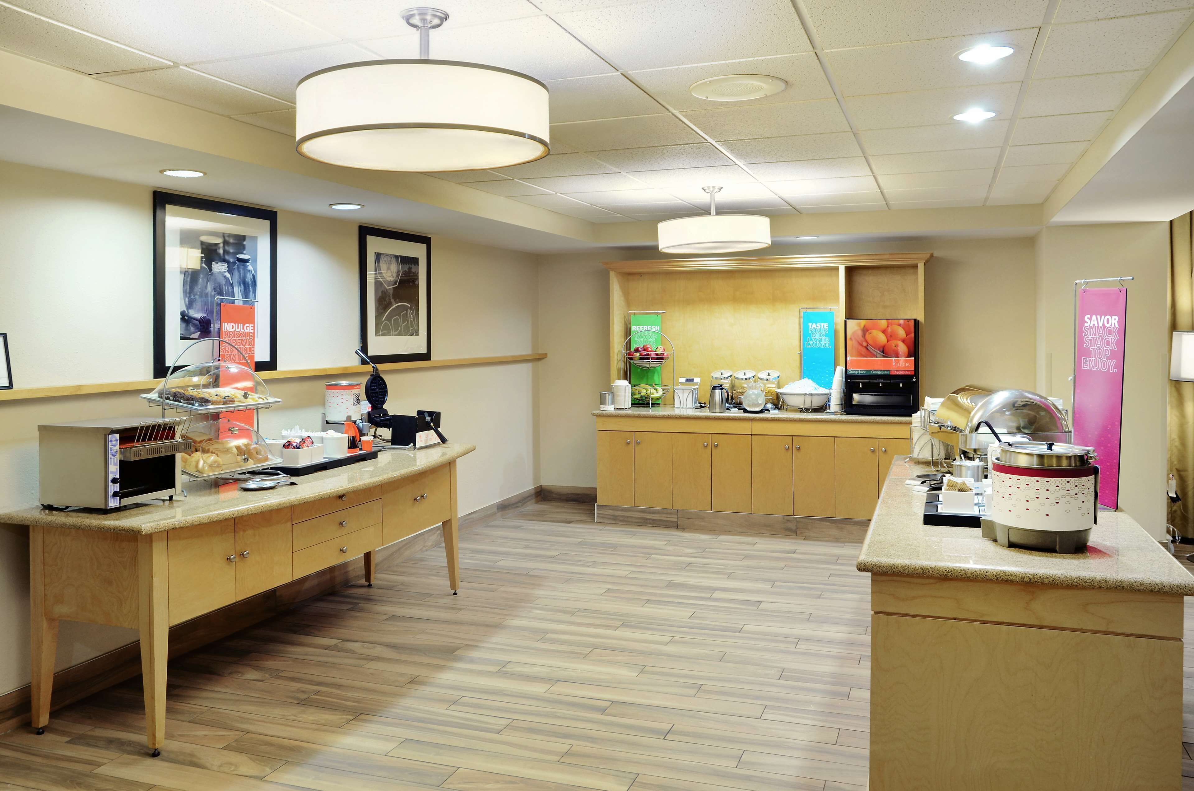 Um saguão de hotel com balcão de recepção, cantinho do café e balcão com exposição de comida.